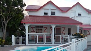 Une maison à deux étages avec une piscine, des balustrades blanches et un toit rouge.