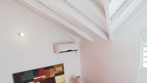 Une chambre à coucher avec un lit, une table de chevet, une lampe, un climatiseur et une fenêtre.
