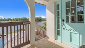 Een turquoise deur met een "hello" bord, een balkon met een leuning, en uitzicht op een meer en begroeiing.