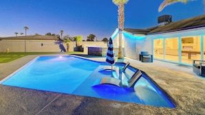 Ein Swimmingpool mit einer Palme, Liegestühlen und einer überdachten Terrasse.