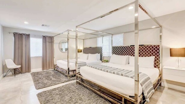 Uma cama de dossel com colcha listrada em branco e cinza, uma mesa de cabeceira com abajur e uma cadeira em um quarto de hotel moderno.
