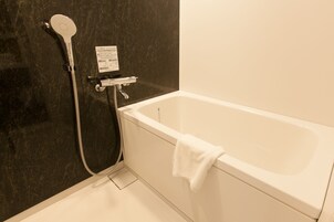Un bagno con una vasca da bagno bianca, un soffione flessibile e un asciugamano appeso a lato.