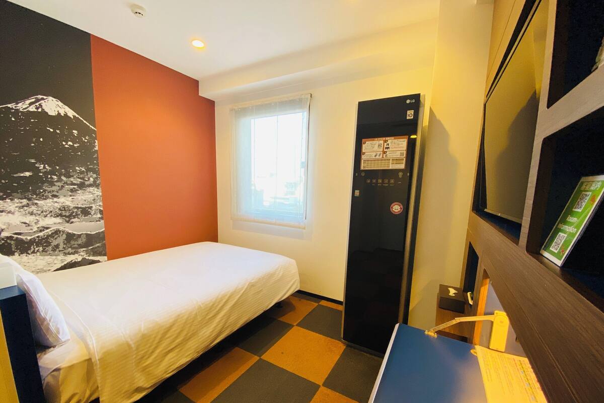 Ein Hotelzimmer mit Bett, Fenster, Kühlschrank und Flachbildfernseher.