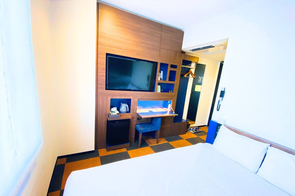 Ein Hotelzimmer mit einem Bett, einem Schreibtisch mit Stuhl, einem Fernseher und einem Kleiderschrank.