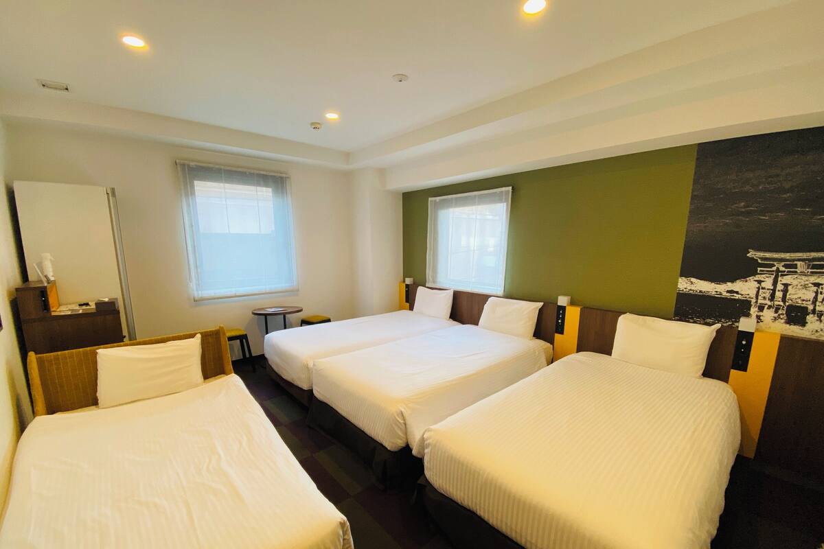 Ein Hotelzimmer mit drei Einzelbetten, einem kleinen Tisch und einem Stuhl.