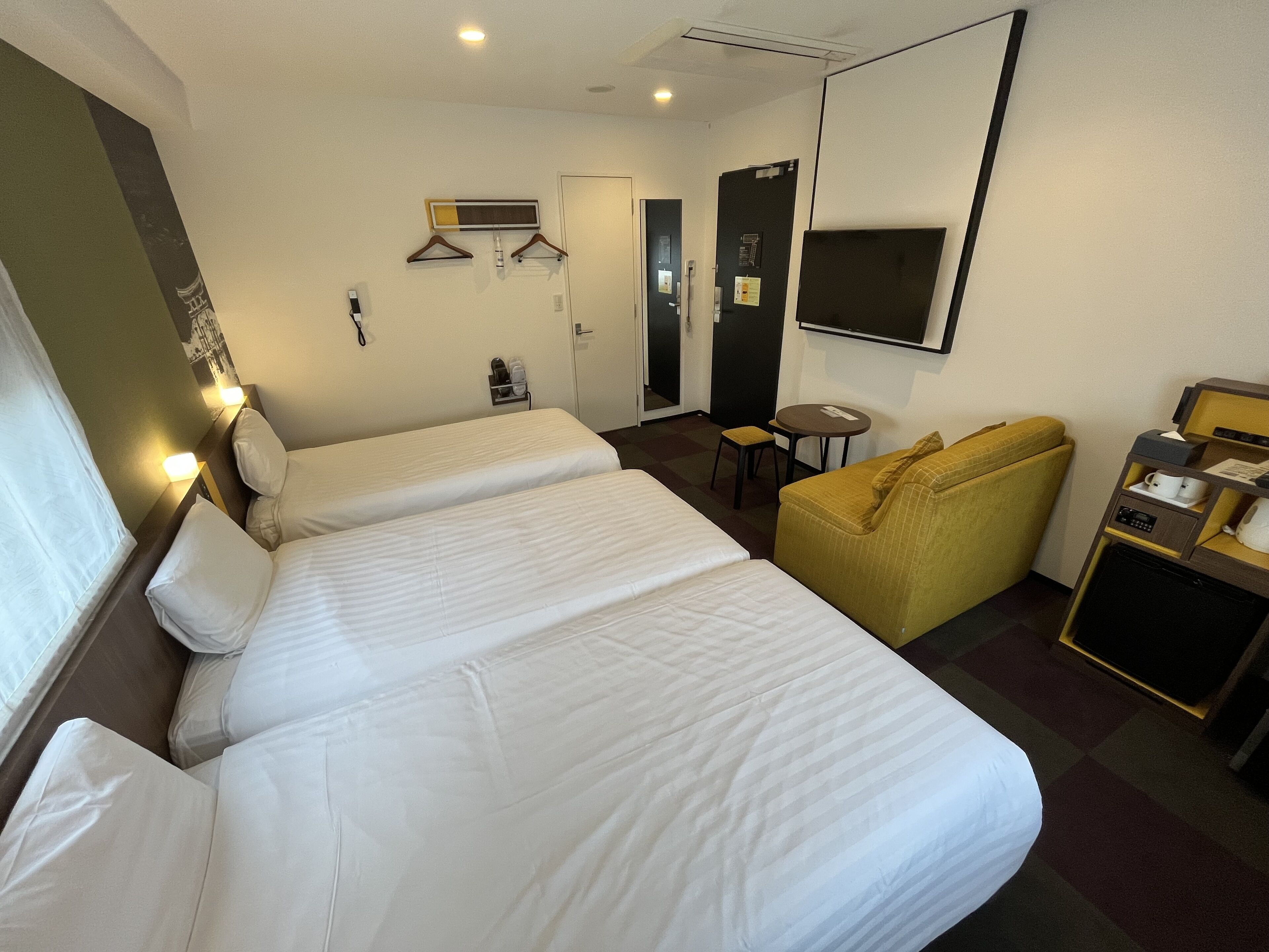 A hotel room with two beds, a sofa, a small table, a TV, and a minibar.