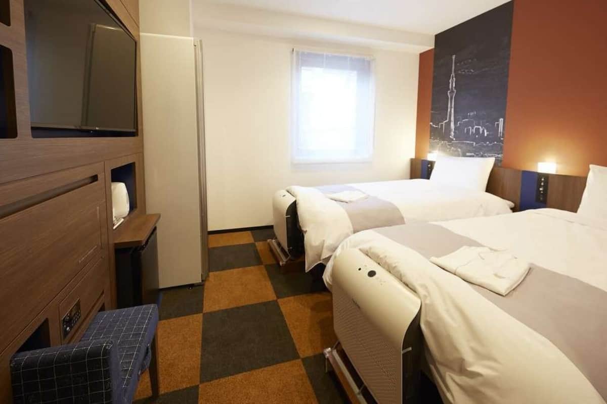 Ein Hotelzimmer mit zwei Betten, einem Fernseher, einem Fenster und Blick auf die Stadt.