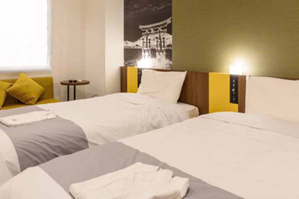 Ein Hotelzimmer mit zwei Betten, einem Schlafsofa, einem kleinen Tisch und einer Wandleuchte.