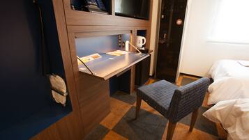 A compact hotel room with a small desk, a chair, and a bed.