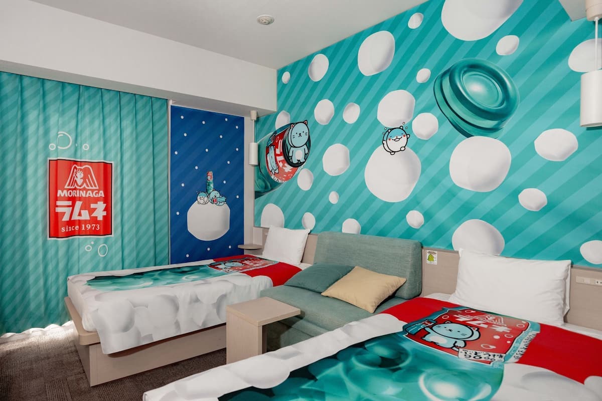 Ein Hotelzimmer mit zwei Betten, einem blauen Vorhang, einer Wand mit Zeichentrick-Schneemännern und dem Morinaga-Logo.