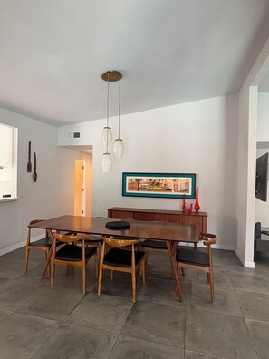 A dining area with a wooden table and chairs, pendant lights, a framed picture, and a cabinet with decorative items. - The Mid-Century Mulligan:  Tahquitz Legends 5th Green Pool Oasis (Palm Springs)