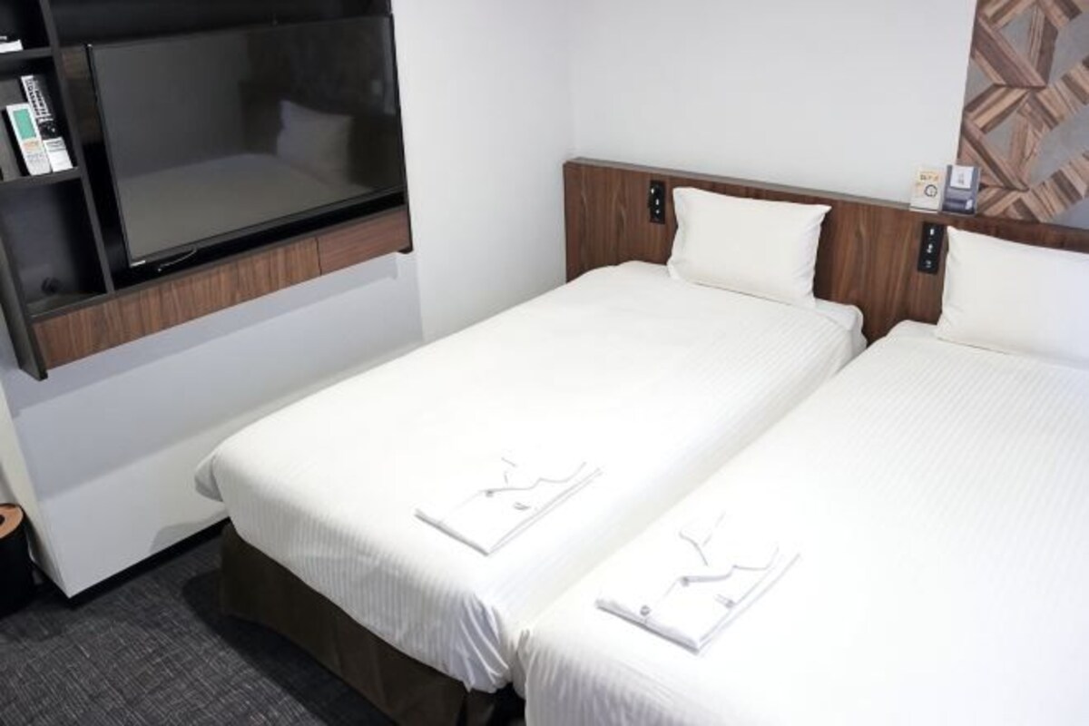 Quarto de hotel com duas camas, uma televisão de tela plana e uma cabeceira de madeira.