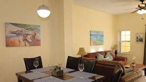 A dining area with a table set for four, a brown leather sofa, and two paintings on the walls. - Family friendly villa, gated community, spa, heated pool, close to theme parks. (Kissimmee)