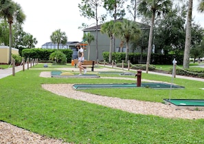 Um campo de mini golfe com área de putting verde, um banco de madeira e palmeiras.