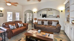 A living room with two brown leather sofas, a wooden coffee table, and a kitchen area with white cabinets and a ceiling fan. - Luxury Living in a Country Setting and Minutes to Lubbock! (Wolfforth)