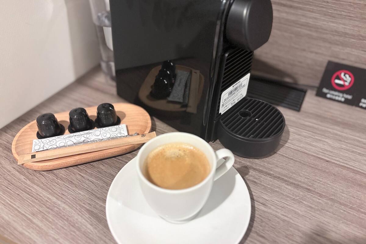 Una cafetera con una taza de café sobre una mesa de madera.