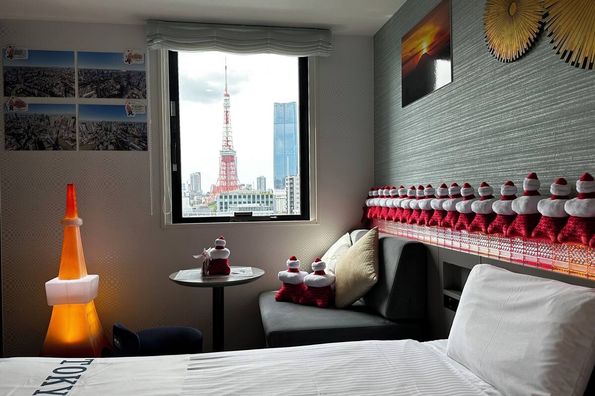 Habitación de hotel con cama, una mesita, ventana con vista a la ciudad y una pared decorada con almohadones rojos y blancos.