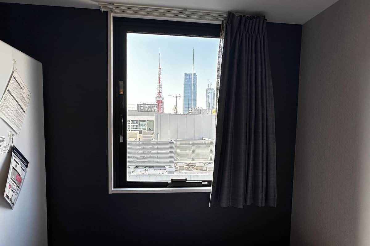 Habitación de hotel con una ventana grande, una cama y vistas a un paisaje urbano que incluye una torre alta.