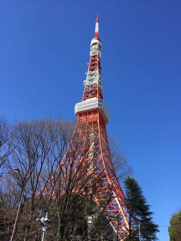 Una torre alta, de color rojo y blanco, con una estructura compleja, rodeada de árboles y un cielo azul despejado.