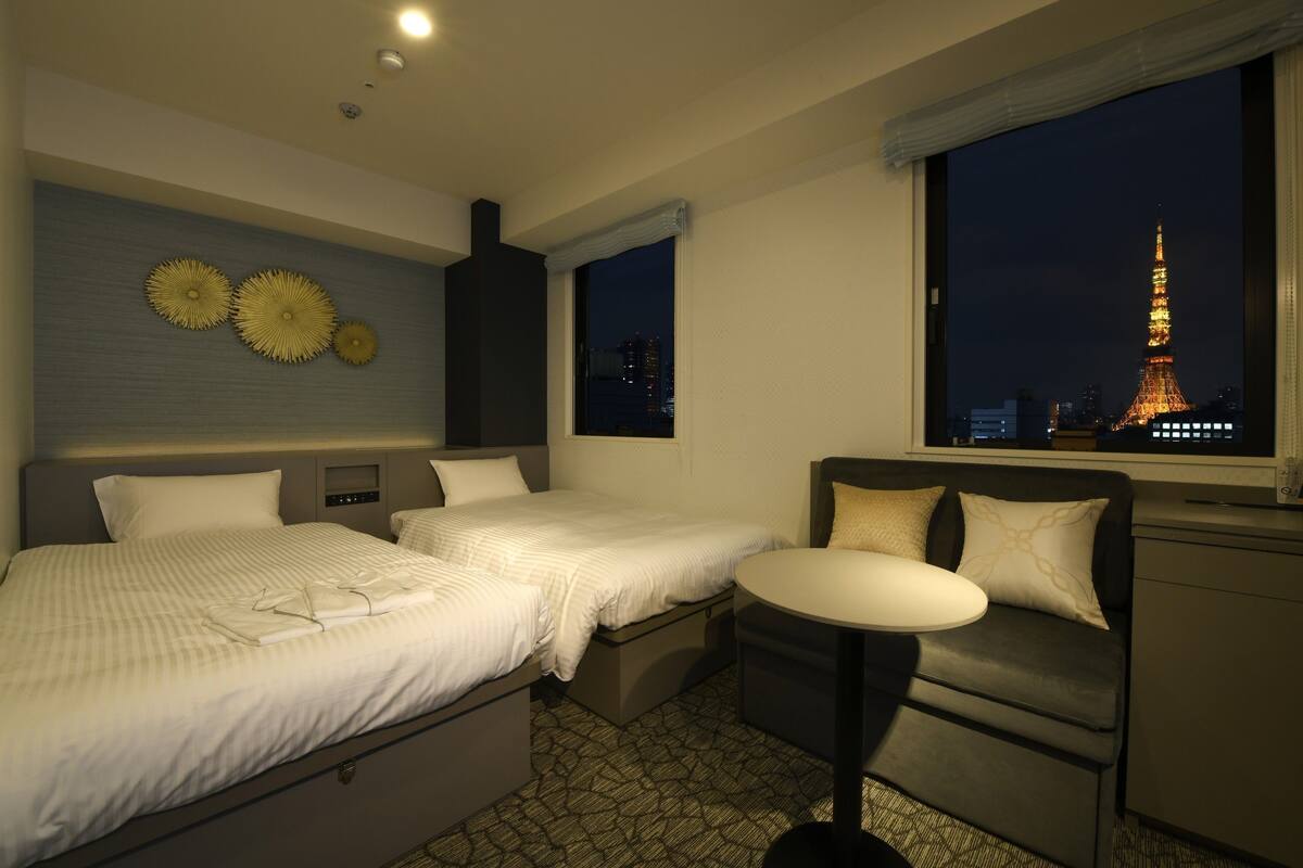 Habitación de hotel con dos camas, una mesita y vistas nocturnas de la Torre Eiffel.