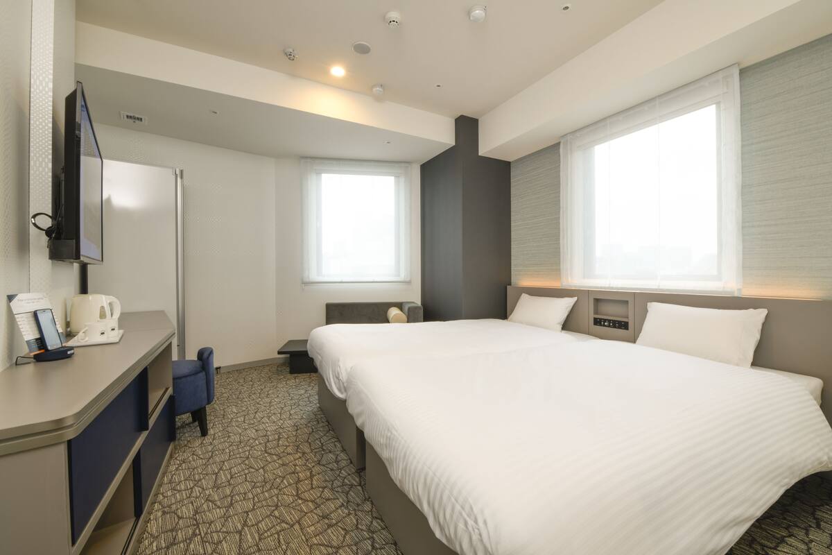 Una habitación de hotel con cama, escritorio, silla, televisión y ventana.