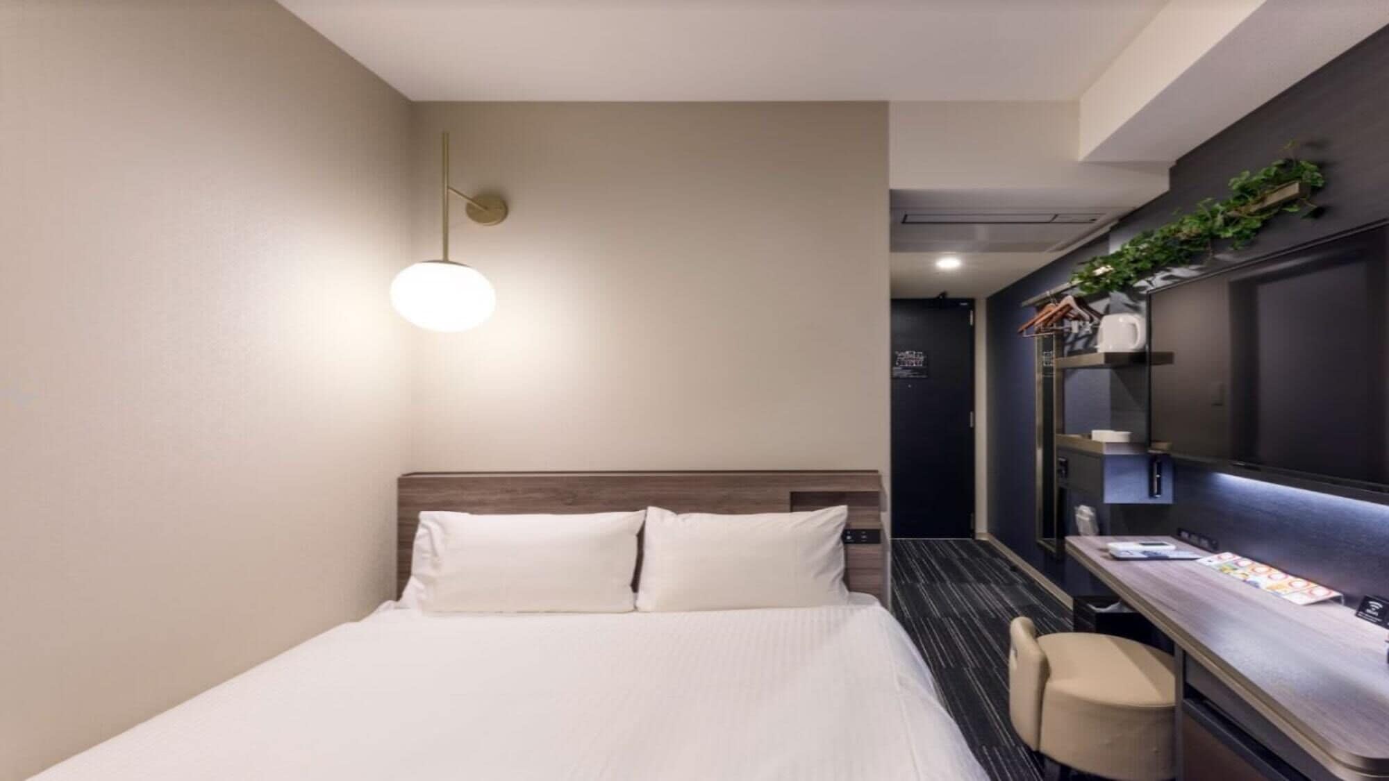 A hotel room with a bed, a desk, a chair, a wall-mounted TV, and a door.