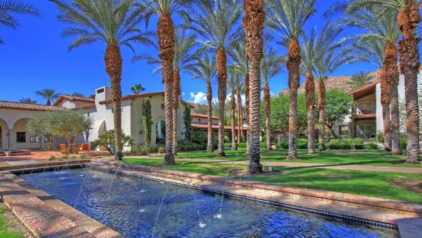 A pool area with palm trees and a building with a tiled roof.