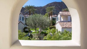 A view through an archway of a residential area with houses, greenery, and a mountain in the background.