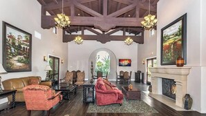 A spacious living room with a high ceiling, wooden beams, a fireplace, and multiple seating areas.