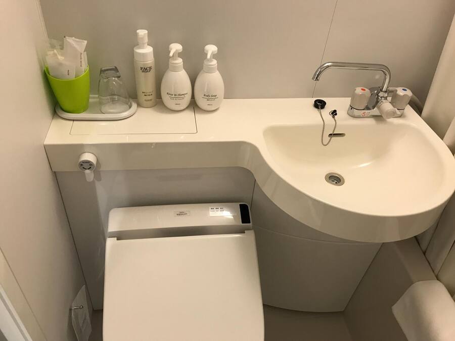 Ein Badezimmer mit Waschbecken, Toilette und Dusche. Auf dem Waschtisch liegen Pflegeprodukte.