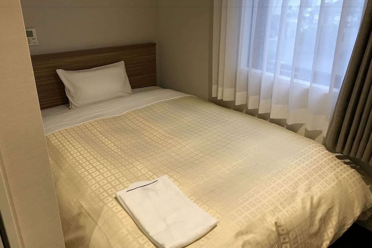 Een hotelkamer met een net opgemaakt bed, een houten hoofdbord en dunne gordijnen.
