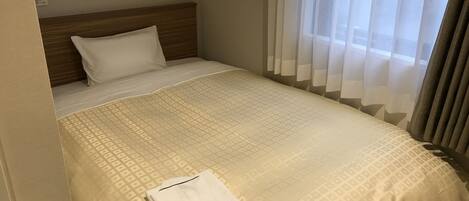 Habitación de hotel con cama bien hecha, cabecera de madera y cortinas traslúcidas.