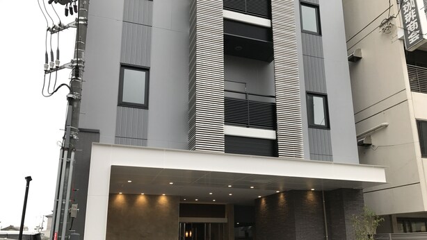 Een modern gebouw met een overdekte ingang, grote ramen en een zichtbare stroomkast.