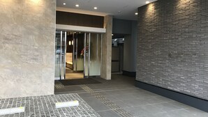 Een moderne hotelentree met een glazen lift, een bakstenen muur en een betegelde vloer.