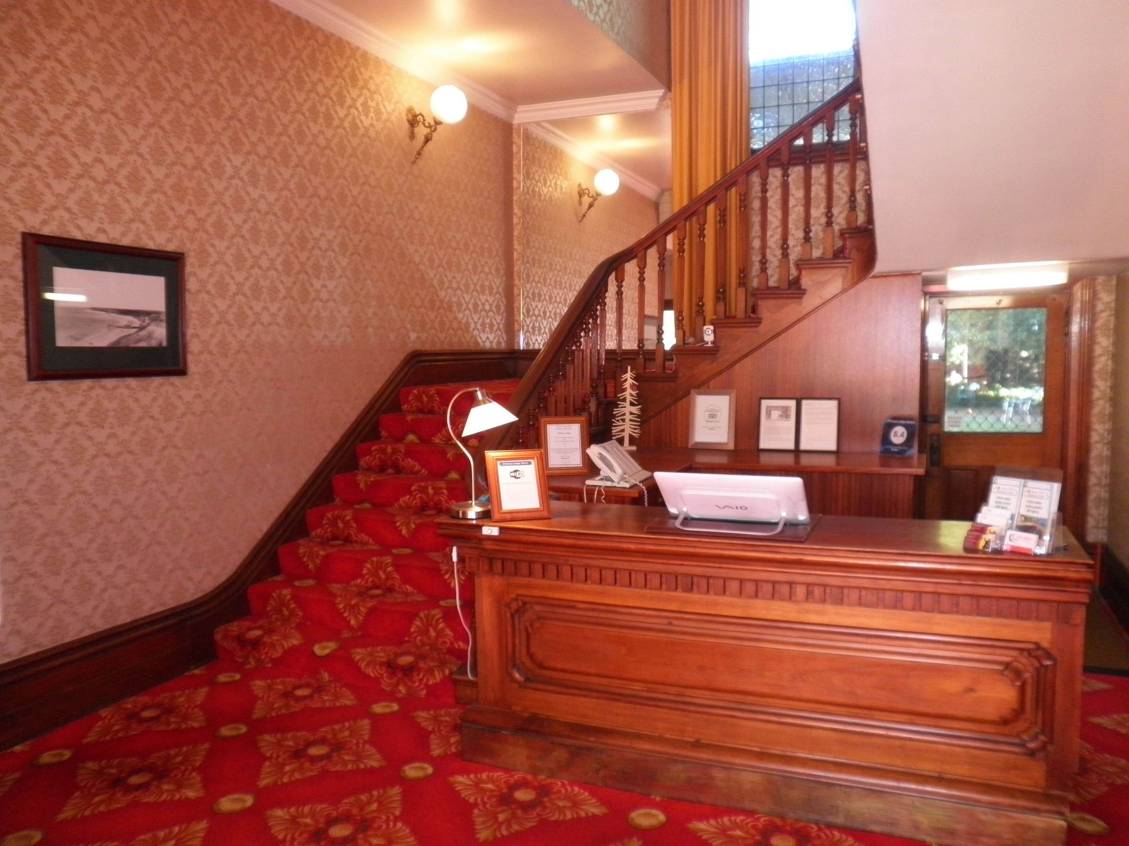 A reception desk with a red carpet, wooden staircase, and framed certificates on the wall.