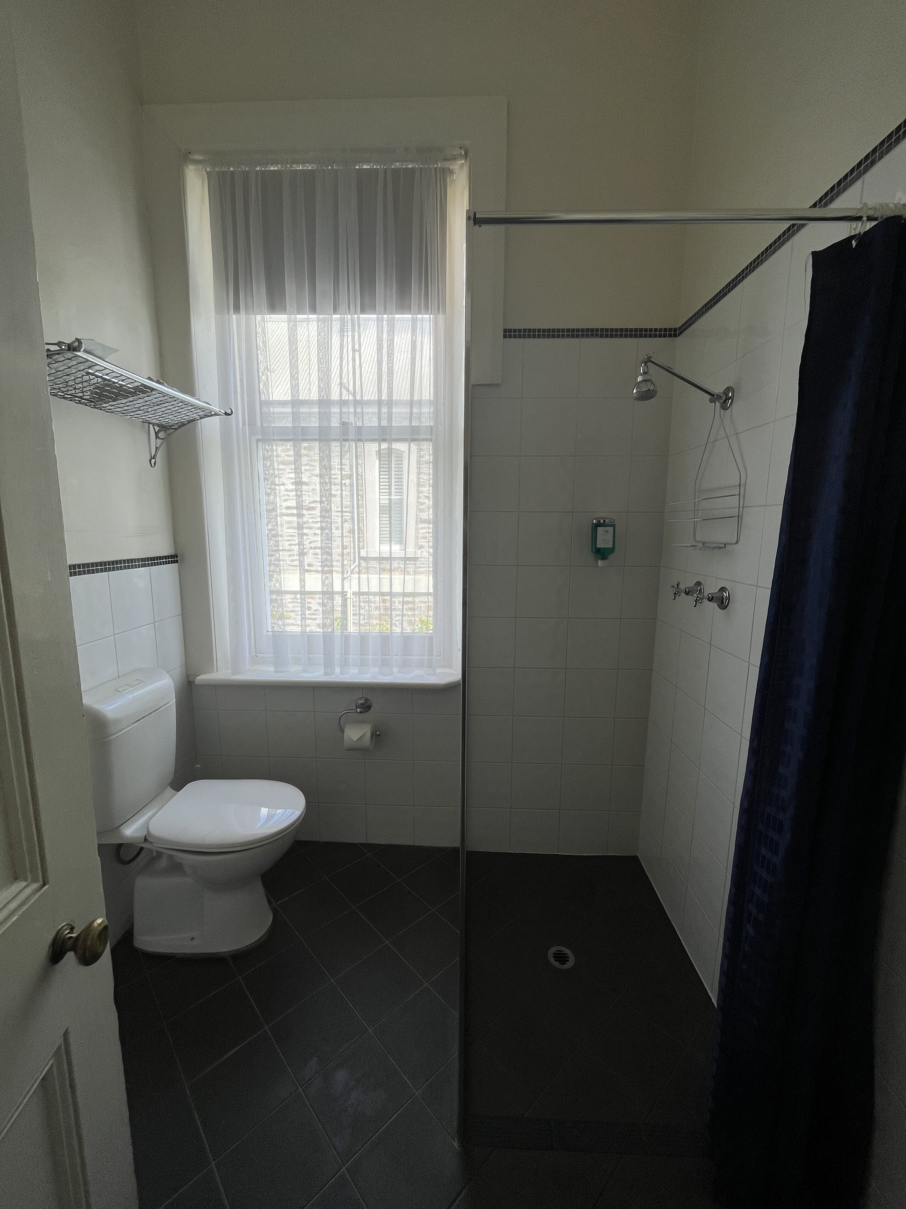 A small, compact bathroom with a toilet, a shower, and a window.