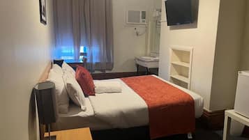 A hotel room with a bed, a bedside table, a TV mounted on the wall, a window with curtains, and a bathroom with a sink and mirror.