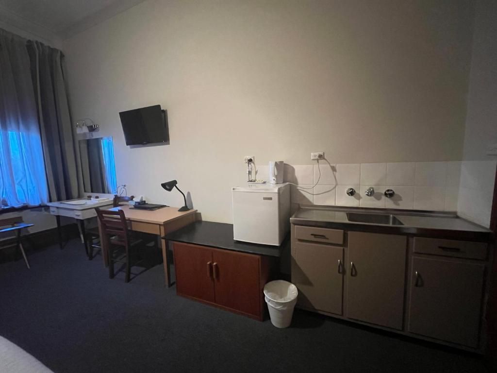 Habitación de hotel compacta con kitchenette, escritorio, silla, televisor montado en la pared y ventana con cortinas.