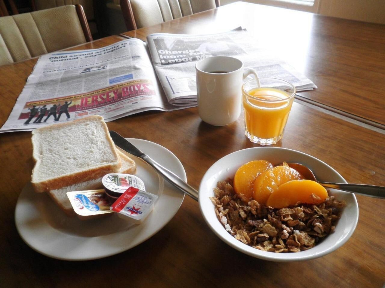 A breakfast setting with toast, cereal, orange juice, and a newspaper on a wooden table.