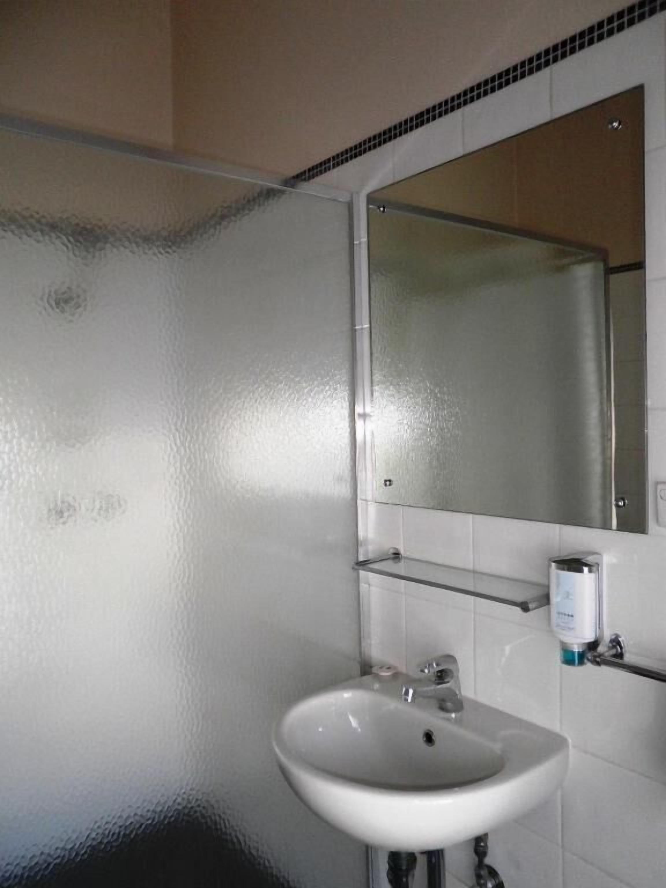 A bathroom with a white sink, a mirror, and a glass shelf.