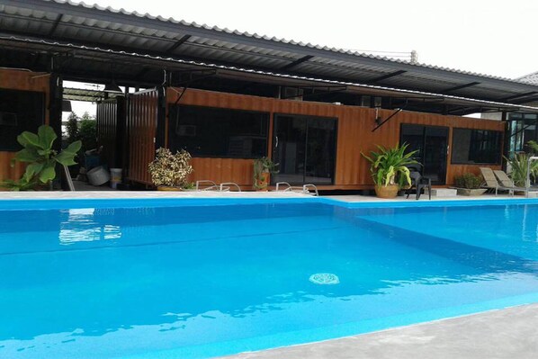 A modern poolside area with a clear blue pool, wooden deck, and potted plants.