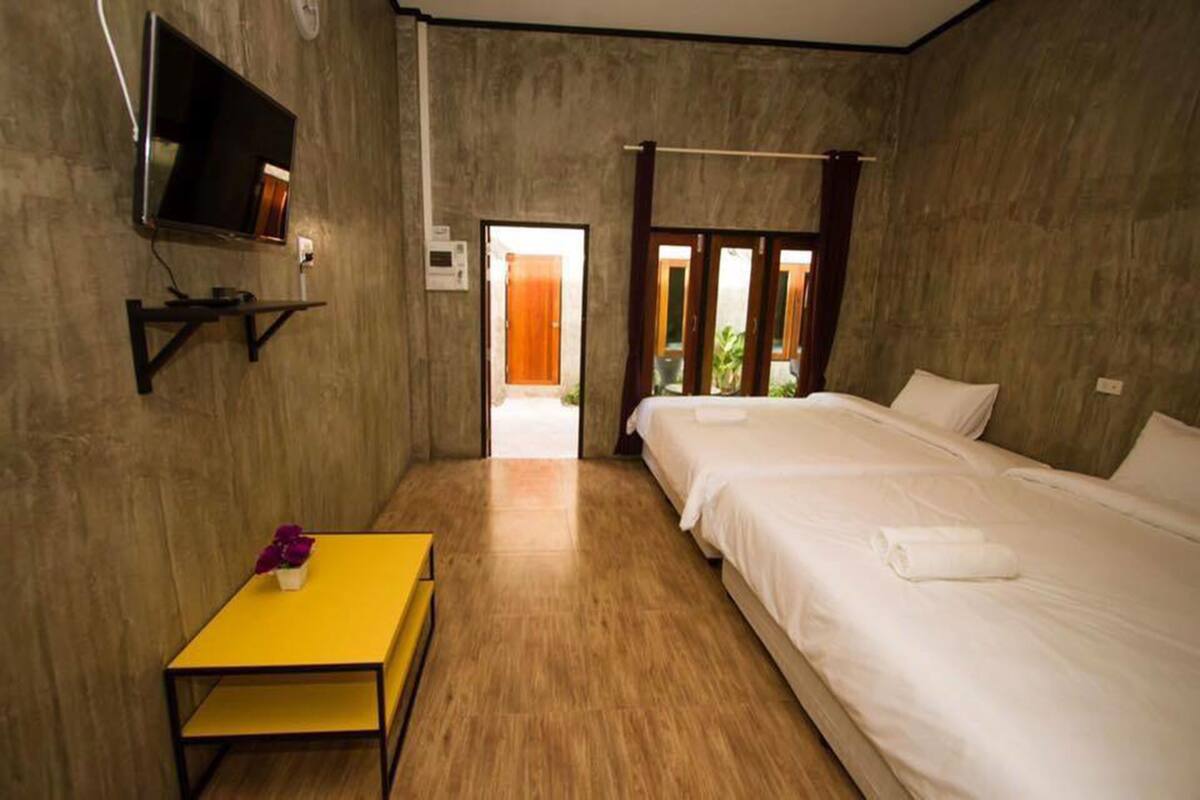 A hotel room with a bed, a TV mounted on the wall, a small table with a vase, and a wooden floor.