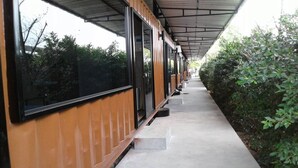 A covered walkway with large windows and a concrete path, flanked by greenery. - Rintara Riverside Resort (Klaeng)