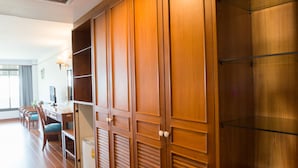 A hotel room with wooden flooring, a desk with a chair, a bed, and a wardrobe with multiple compartments. - KU Home Hotel (Bangkok)