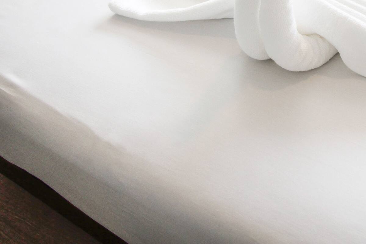 Un lit bien fait, avec un drap blanc et une serviette blanche pliée en forme de cygne.