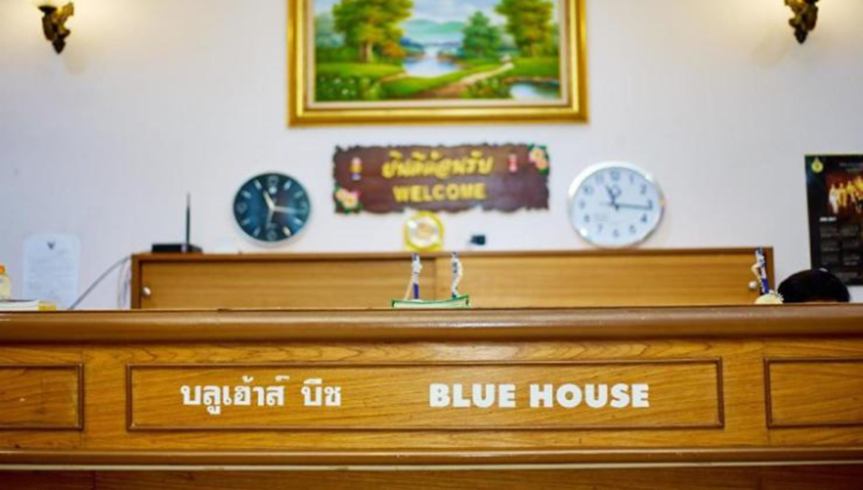 Un comptoir d’accueil avec une enseigne indiquant « BLUE HOUSE » et une pancarte de bienvenue au-dessus.