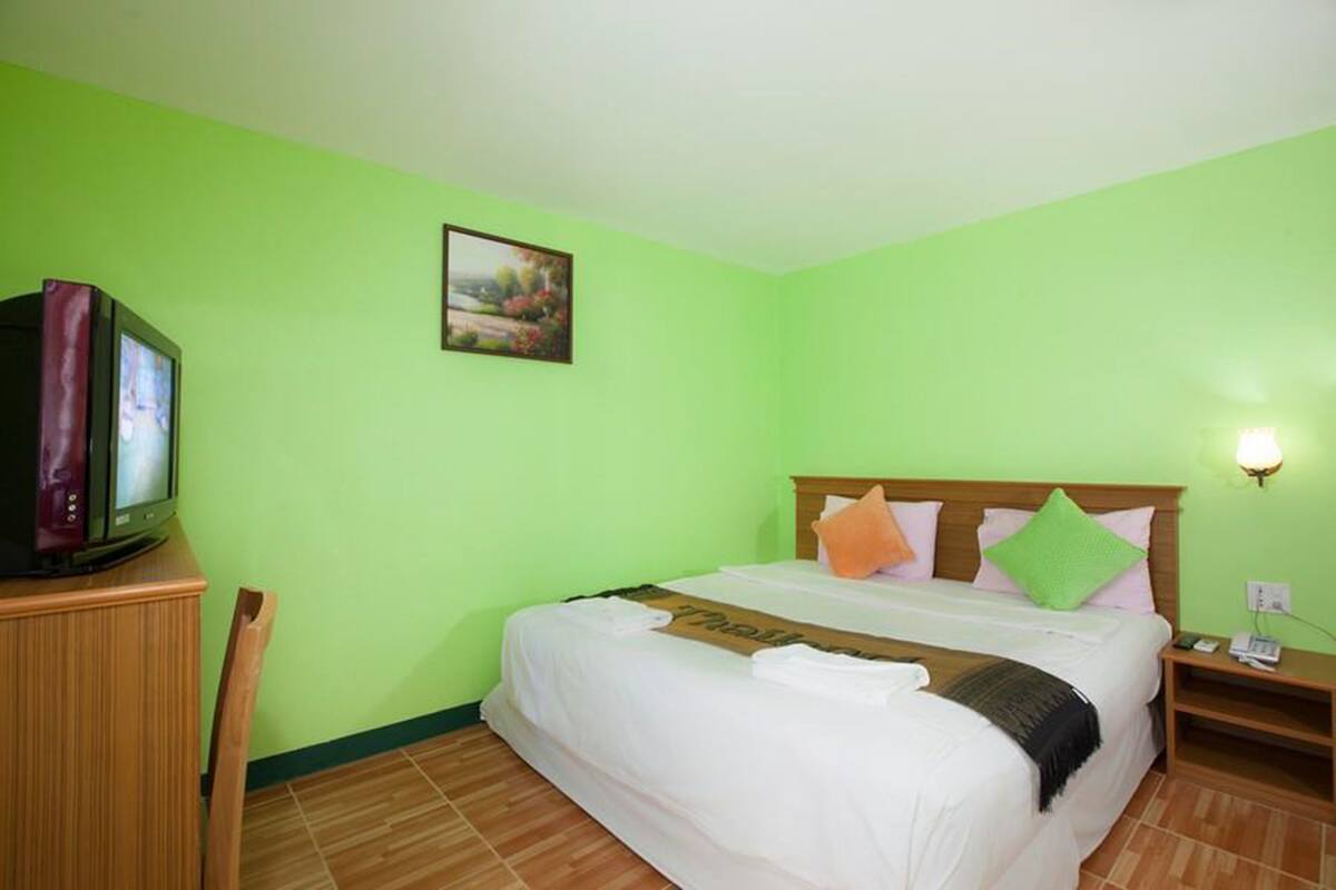 A hotel room with a bed, a television, a nightstand, a lamp, and a painting on the wall.