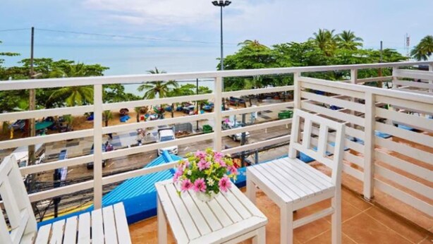 A balcony with white railings, a blue chair, a white table, and a vase of pink flowers. - Blue House Beach (Pattaya)