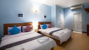 A hotel room with two beds, each with a wooden headboard, white bedding, and decorative pillows. There is a bedside table with a lamp, a wall-mounted air conditioner, and a door with a white handle. - Blue House Beach (Pattaya)