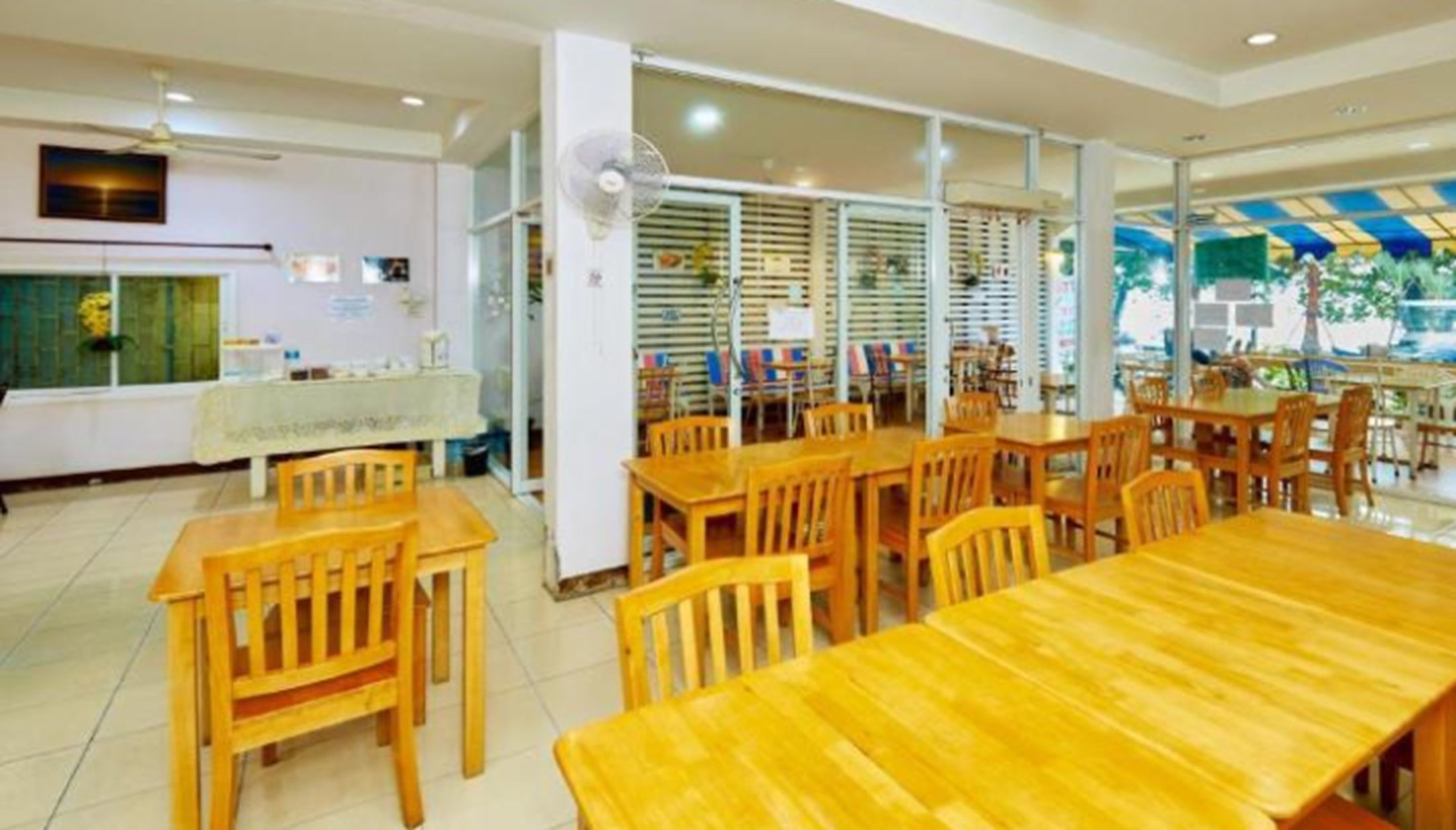 A dining area with wooden tables and chairs, a fan, and a view of the outdoors.